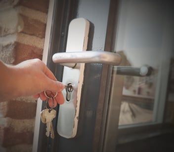 A hand holding a set of keys opening a door with an interchangeable core